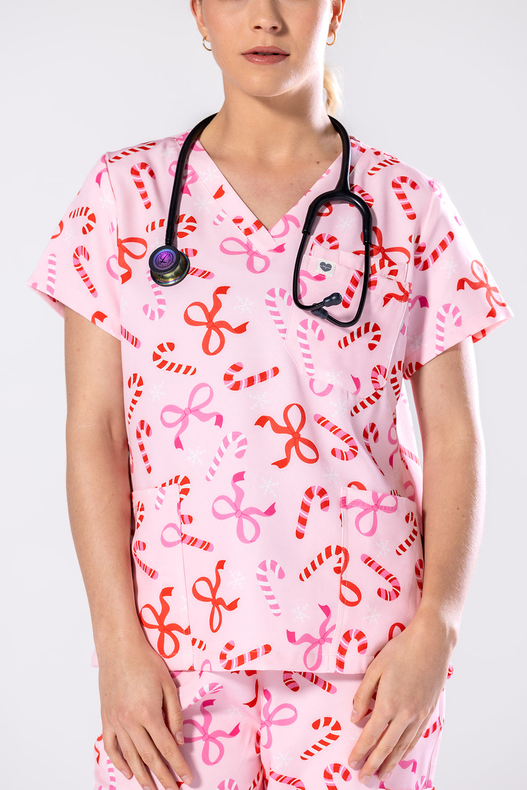 Person wearing a pink medical scrub top with candy cane and bow pattern on a white background